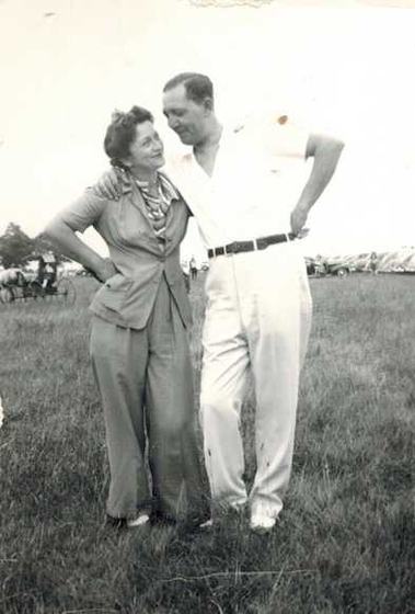 Harold and Mae, arms around each other, on a grass field.