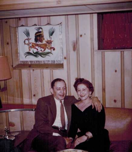 Harold and Mae on a sofa in a wood-paneled room.