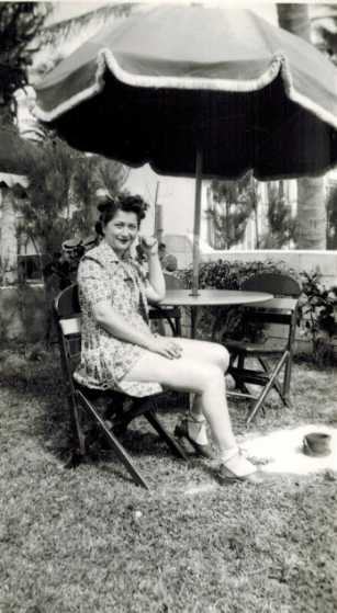 Mae at a table under a big umbrella on a lawn.
