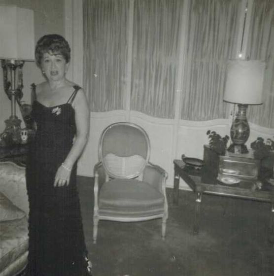 Mae in a long black gown in a living room.