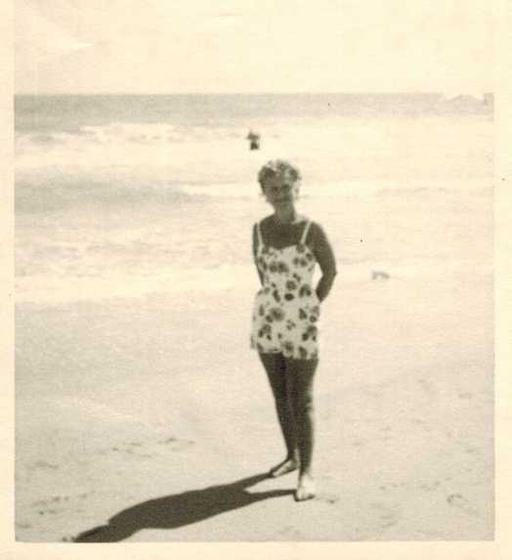 Mae in a floral swimsuit at the edge of the surf.
