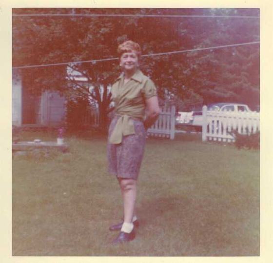 Mae in a green blouse in a backyard with a picket fence.