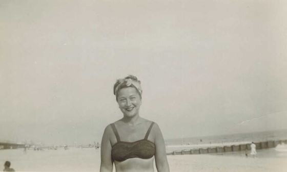 Mae in a headscarf on a beach with a jetty.