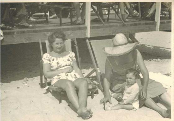 Two women on the beach, one holding a toddler. Mae is on the left.