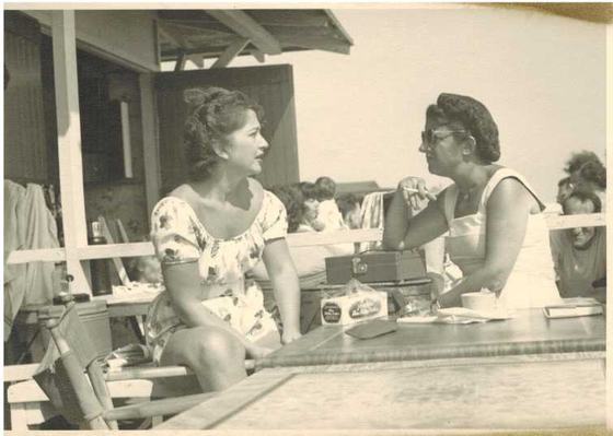 Two women talking at a boardwalk table. Mae is on the left.