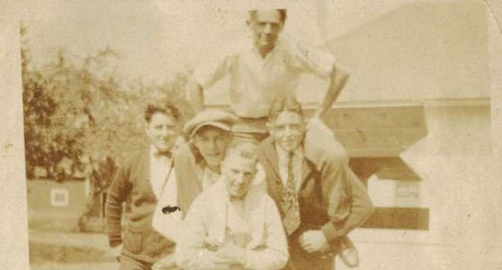 Five young men stacked in a pyramid in front of a house.