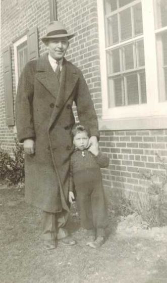 Harold in a long overcoat and fedora, with his son Warren as a small boy in front of him, beside a brick house.