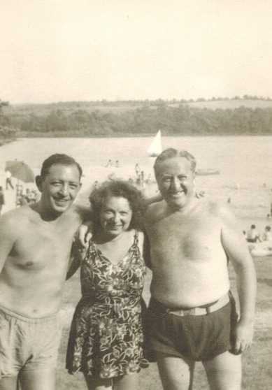 A woman between two shirtless men at a lake shore, arms around each other, with a sailboat behind them. One of the men is believed to be Harold, and the other perhaps Tootsie.